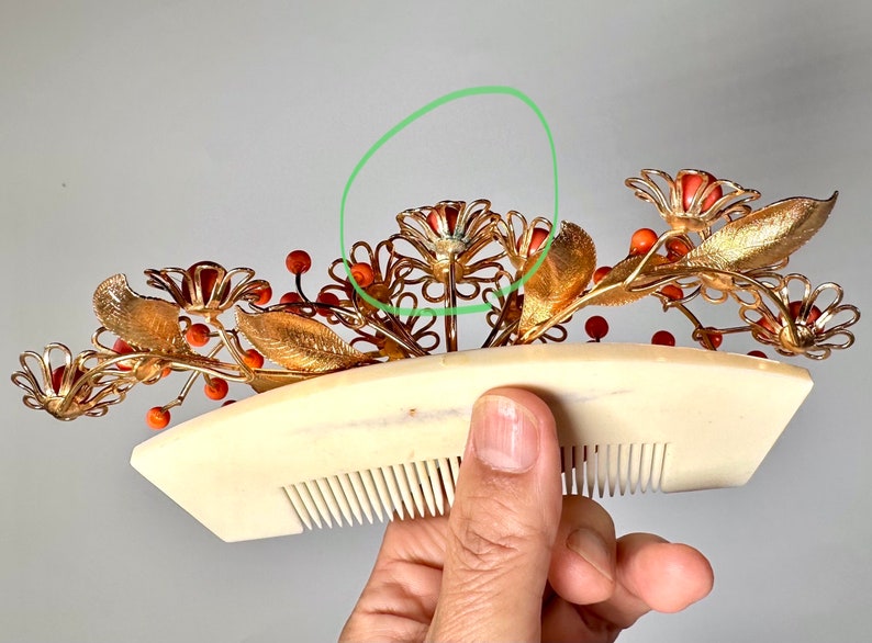 Op de afbeelding: Gouden haar kam met koraal gekleurde bloemen en bladeren. De kam is versierd met kleine rode kralen.