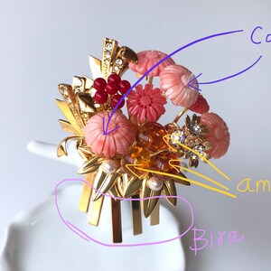 Puede incluir: Un peine de pelo dorado con un dise&ntilde;o floral. Las flores est&aacute;n hechas de coral, &aacute;mbar y piedras rosas. El peine tiene un dise&ntilde;o decorativo con hojas doradas y una perla.