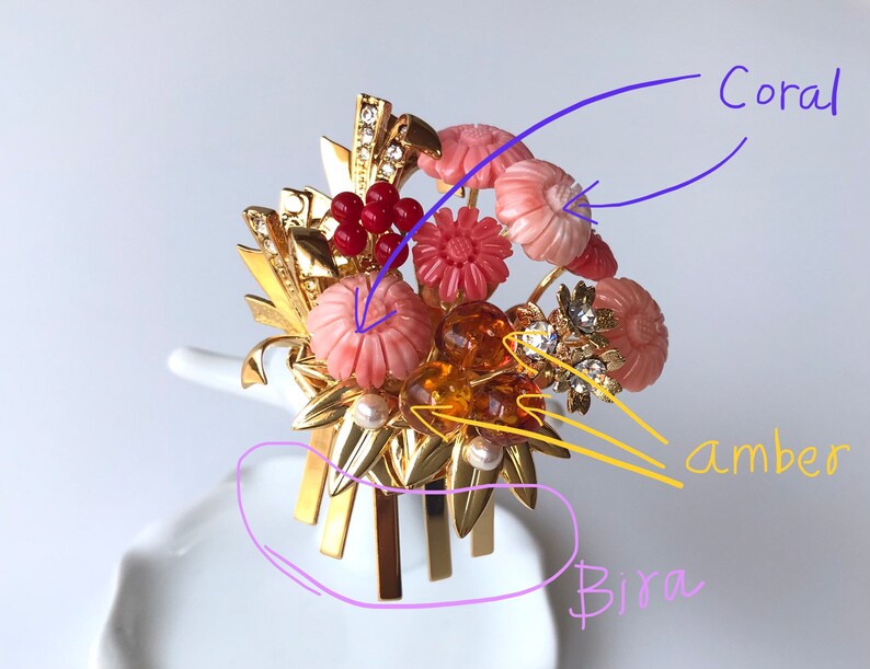 Puede incluir: Un peine de pelo dorado con un dise&ntilde;o floral. Las flores est&aacute;n hechas de coral, &aacute;mbar y piedras rosas. El peine tiene un dise&ntilde;o decorativo con hojas doradas y una perla.