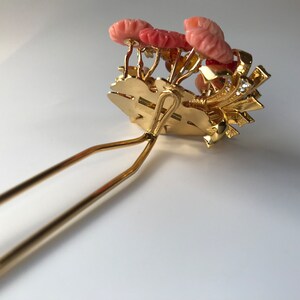 Puede incluir: Peine de pelo dorado con un grupo de flores de coral rosa y diamantes de imitaci&oacute;n. El peine tiene un dise&ntilde;o de doble punta.