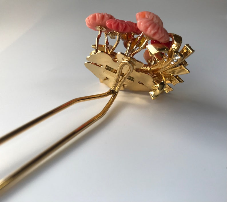 Puede incluir: Peine de pelo dorado con un grupo de flores de coral rosa y diamantes de imitaci&oacute;n. El peine tiene un dise&ntilde;o de doble punta.