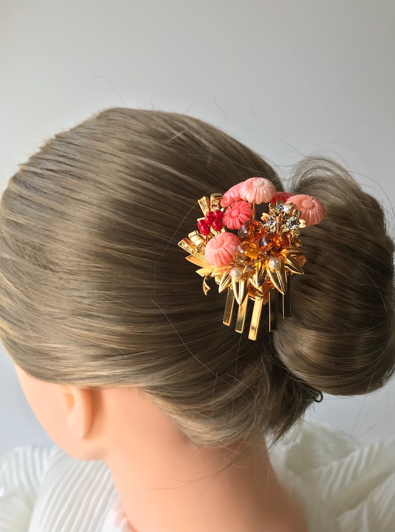 Puede incluir: Un peine de pelo dorado con un grupo de flores rosas y rojas, perlas y pedrer&iacute;a. El peine est&aacute; dise&ntilde;ado para sujetar un mo&ntilde;o o un recogido.