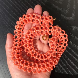 Puede incluir: Un collar de cuentas de color coral con un cierre dorado. El collar est&aacute; hecho de peque&ntilde;as cuentas redondas dispuestas en un patr&oacute;n delicado. El cierre es redondo con una piedra de color coral en el centro.