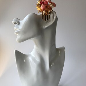 Puede incluir: Un peine de pelo dorado con detalles de flores rosas y blancas. El peine est&aacute; decorado con pedrer&iacute;a y perlas.