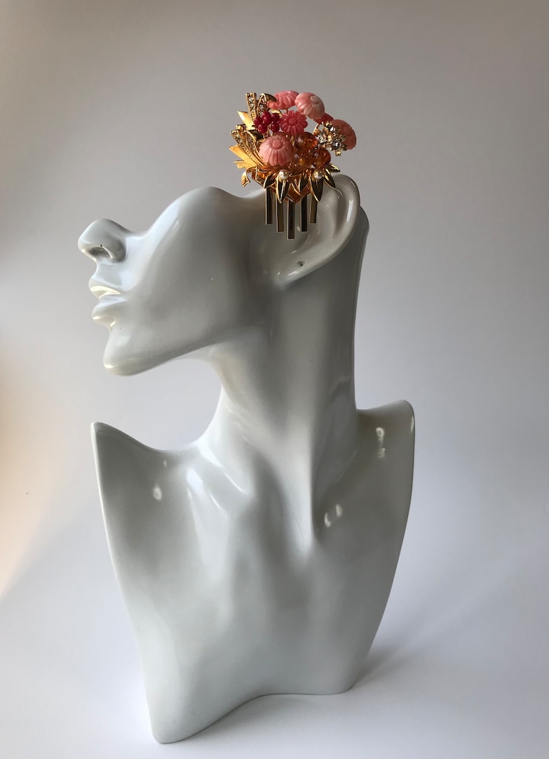 Puede incluir: Un peine de pelo dorado con detalles de flores rosas y blancas. El peine est&aacute; decorado con pedrer&iacute;a y perlas.