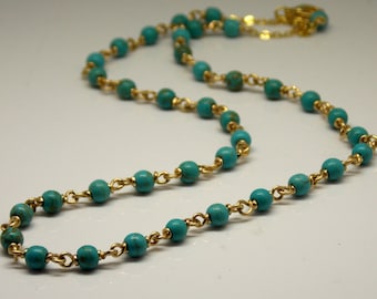 May include: A turquoise and gold necklace with small round beads. The necklace is made of a gold chain with turquoise beads strung on it.