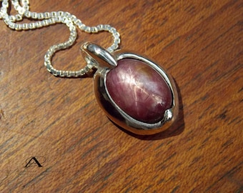 May include: A silver pendant necklace featuring a pink star ruby gemstone set in a silver oval bezel.