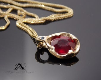 May include: A gold pendant necklace featuring a red gemstone and a small black diamond. The pendant is teardrop shaped and has a textured surface.