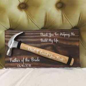 May include: A wooden sign with a hammer attached to it. The sign has the text "Thank You For Helping Me Build My Life Dad, I Loved You First Father of the Bride 06/16/2018" written on it.