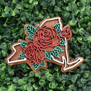 May include: A wooden cutout of the state of New York with a red and green floral design. The flowers are roses with leaves.