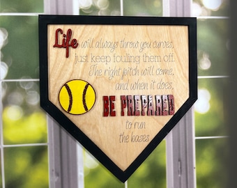 May include: A wooden home plate with a black frame and a yellow baseball. The home plate has the text "Life will always throw you curves, just keep fouling them off. The right pitch will come, and when it does, BE PREPARED to run the bases".