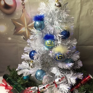 May include: A white artificial Christmas tree decorated with blue and silver ornaments, some with the letters "AEA" in yellow. The tree is surrounded by wrapped gifts and Christmas crackers.