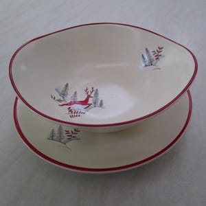 May include: Cream-coloured serving bowl and plate set with a red rim. The bowl features a red deer leaping through a forest scene. The plate also has a forest scene with a red rim. A festive, seasonal design.