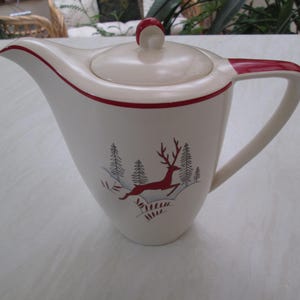 May include: Cream ceramic creamer with a lid and handle, featuring red trim. The creamer has a forest scene with a red deer and trees. A classic piece for serving cream or other liquids.