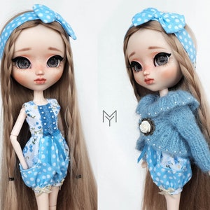 Può includere: Due bambole con lunghi capelli biondi che indossano abiti blu e bianchi. Una bambola indossa un maglione blu con una spilla a forma di fiore bianco e una gonna a pois blu e bianchi. L'altra bambola indossa un vestito a fiori blu e bianchi con una gonna a pois blu e bianchi.