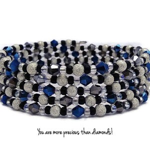Puede incluir: Un brazalete de múltiples hilos hecho de cuentas plateadas, negras y azules. Las cuentas son una mezcla de cuentas redondas, facetadas y brillantes.