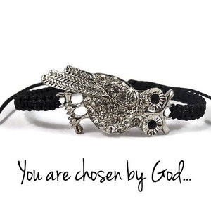 Op de afbeelding: Zwart gevlochten armband met een zilveren uil bedel met heldere strass steentjes en zwarte ogen. De armband heeft een zilveren sluiting en de tekst "You are chosen by God..." staat onder de afbeelding.
