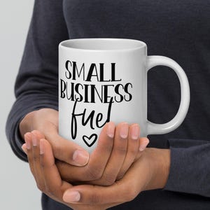 Könnte beinhalten: Weiße Keramik-Kaffeetasse mit schwarzem Text, der "SMALL BUSINESS fuel" lautet, mit einem kleinen Herzsymbol unter dem Text.
