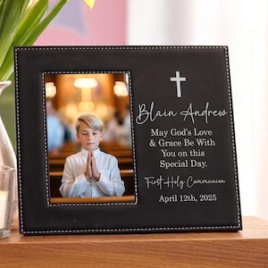 May include: Black leather picture frame with a photo of a boy in a church. The frame has a white cross and text that reads "Blain Andrew, May God's Love & Grace Be With You on this Special Day. First Holy Communion April 12th, 2025."