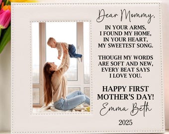 May include: A white photo frame with a stitched border. The frame has a photo of a mother holding her baby up in the air. The text in the frame reads "Dear Mommy, In your arms, I found my home, In your heart, My sweetest song. Though my words are soft and new, Every beat says I love you. Happy First Mother's Day! Emma Beth 2025"
