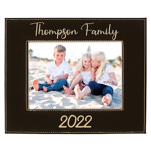 May include: A brown leather picture frame with a stitched border. The frame has a photo of three children on a beach. The text "Thompson Family" is written in gold above the photo and "2022" is written in gold below the photo.
