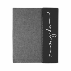 May include: A gray and black fabric binder with the word "angela" written in white cursive on the black side.