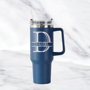 May include: A navy blue insulated tumbler with a handle and a clear lid. The tumbler features a large silver letter "D" with the name "DANIEL" in a horizontal bar across the middle. A clear straw is inserted into the lid.