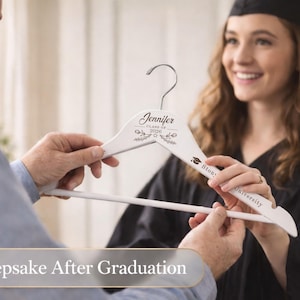 May include: White wooden hanger with the name "Jennifer" and "Class of 2026" printed on it. The hanger is being held by two people, one of whom is wearing a graduation gown and cap. The text "A Keepsake After Graduation" is at the bottom.