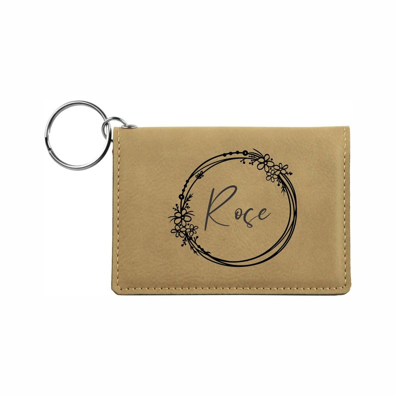 May include: A tan leather keychain with a silver key ring and a black floral wreath design with the name "Rose" inside.