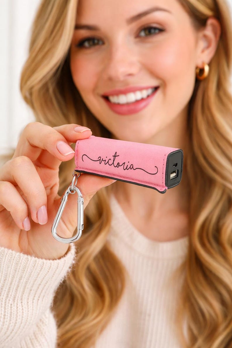 Pink personalized power bank keychain charger with engraved name, compact portable phone charger clipped to keys and charging a smartphone, travel friendly tech accessory gift.