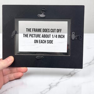 May include: Black picture frame with a white paper insert that reads "The frame does cut off the picture about 1/4 inch on each side".