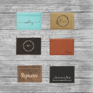 May include: Six personalized leather keychains with different names and designs. The keychains are brown, black, tan, and blue. The names on the keychains are Ashley, Rose, Robin, Stephanie, and Jennifer.