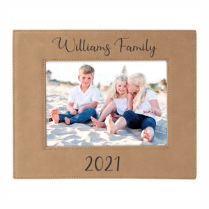 May include: A tan leather photo frame with a stitched border. The frame has a photo of three children on a beach. The text "Williams Family" is printed at the top of the frame and "2021" is printed at the bottom.
