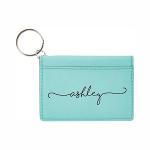 May include: A light blue leather keychain with a silver key ring and the name "ashley" written in black cursive.