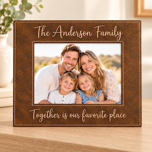 May include: A rectangular brown faux leather picture frame with white stitching. The top text reads The Anderson Family and the bottom text reads Together is our favorite place. A photograph of a family of four is displayed inside.