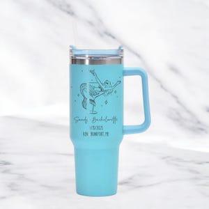 May include: A light blue tumbler with a handle and a lid, featuring a mermaid design and the text "Sandy Bachelorette 1/15/2025 KEN BUNKPOT, ME". The tumbler includes a straw.