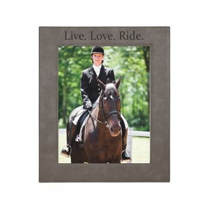 May include: A grey leather picture frame with a black and white photograph of a person riding a horse. The frame has the text "Live. Love. Ride." engraved on the top.
