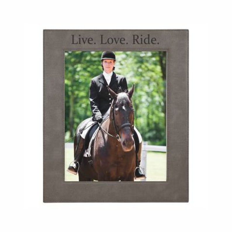 May include: A grey leather picture frame with a black and white photograph of a person riding a horse. The frame has the text "Live. Love. Ride." engraved on the top.