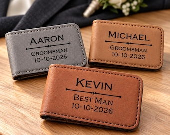 May include: Three rectangular leather money clips in gray, tan, and brown. Each clip is engraved with a name, a title, and the date 10-10-2026. The clips are labeled Aaron Groomsman, Michael Groomsman, and Kevin Best Man with decorative lines.