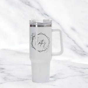 May include: White insulated tumbler with a handle and a straw. The tumbler features a black floral design around a geometric frame with the name "Cathy" in script. The lid is silver and white.