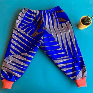 May include: Blue and white patterned trousers with orange cuffs. The trousers have a geometric design with white lines and brown accents.
