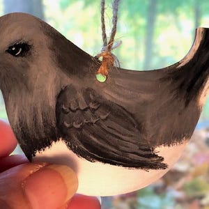 May include: A hand-painted wooden bird ornament with black and white paint. The bird has a small, round body and a long, thin tail. The bird is painted in a realistic style, with details such as feathers and eyes.