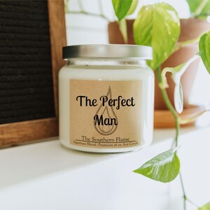 May include: A white soy candle in a glass jar with a silver lid. The label reads "The Perfect Man" above "The Southern Flame" and "Signature Blend | Premium 16 oz. Soy Candle".