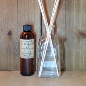 May include: A clear glass reed diffuser bottle with wooden reeds and a brown bottle of reed diffuser refill. The refill bottle has a black cap and a label that reads "The Southern Flame Reed Diffuser Refill Winter Wonderland."