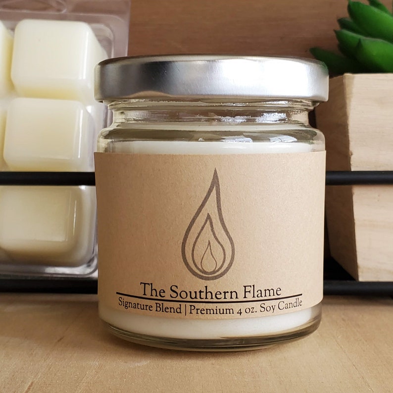 K&ouml;nnte beinhalten: Eine kleine Kerze im Glas mit silbernem Deckel und braunem Etikett. Das Etikett zeigt eine Flammen-Grafik und den Text "The Southern Flame Signature Blend Premium 113g Soy Candle". Die Kerze ist wei&szlig;.