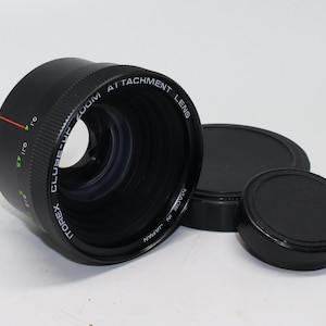 Può includere: Obiettivo aggiuntivo Itorex Close-Up Zoom nero con due copriobiettivo neri. L'obiettivo presenta segni verdi e rossi e la scritta "MADE IN JAPAN". Progettato per la fotografia ravvicinata.