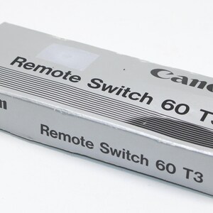 May include: A silver Canon Remote Switch 60 T3 box. The box has black text that reads "Canon Remote Switch 60 T3". The box has a series of black lines on the top and is on a white background.