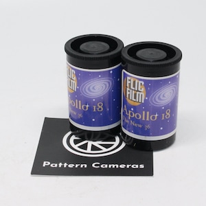 May include: Two black film canisters with blue and white labels that read "FLIC FILM Apollo 18 The New 36". A black card with a white logo and the text "Pattern Cameras" is in front of the canisters. The background is white.