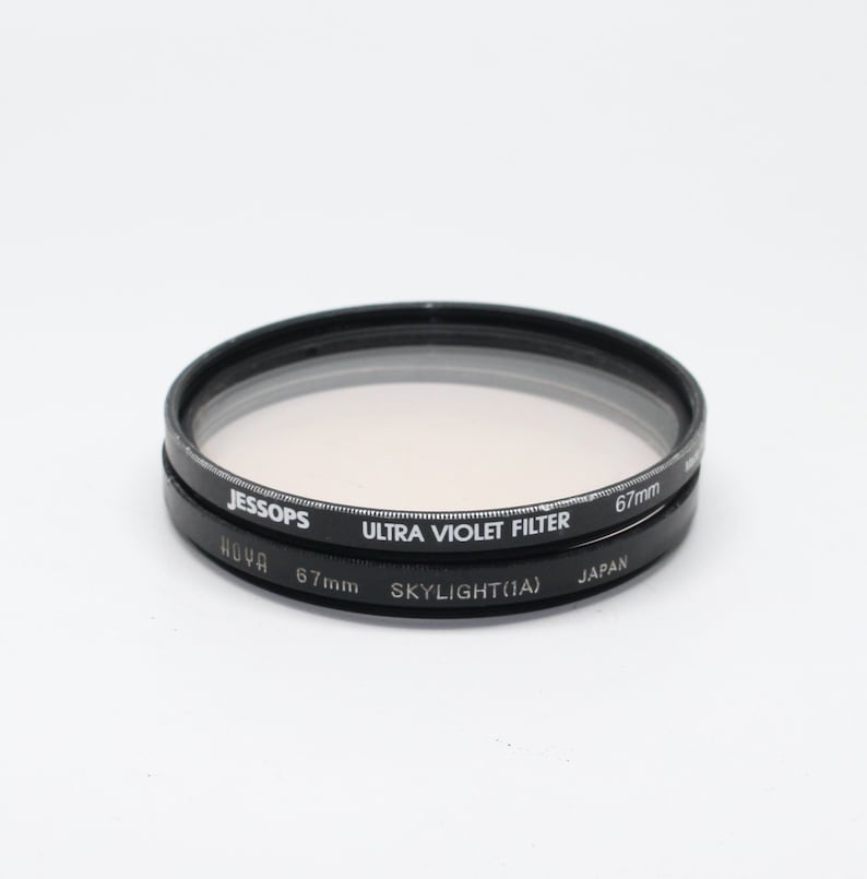 May include: Two black camera lens filters, one labeled "HOYA 67mm SKYLIGHT(1A) JAPAN" and the other labeled "JESSOPS ULTRA VIOLET FILTER 67mm".