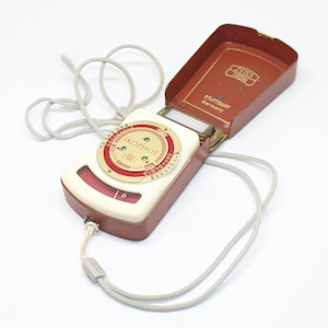 Könnte beinhalten: Vintage Zeiss Ikon Ikophot Belichtungsmesser in einem braunen und cremefarbenen Gehäuse mit rotem Zifferblatt. Das Messgerät hat ein silbernes Kabel und ist geöffnet, wodurch die inneren Komponenten sichtbar werden. Das Gehäuse ist mit "Zeiss Ikon Stuttgart Germany" gekennzeichnet.